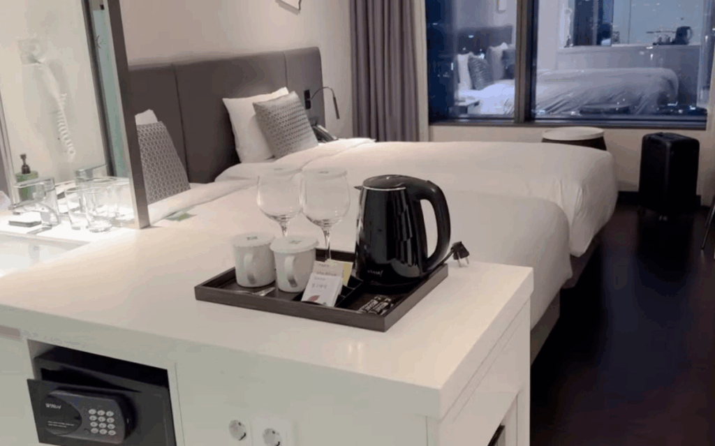 ソウル龍山区イビススタイルズアンバサダーホテルのツインルーム内装 モダンなホワイトインテリア 電気ケトル・セーフティボックス完備 ガラス張りバスルームと都市景観ビュー K-POP推し活に最適な4つ星ビジネスホテル