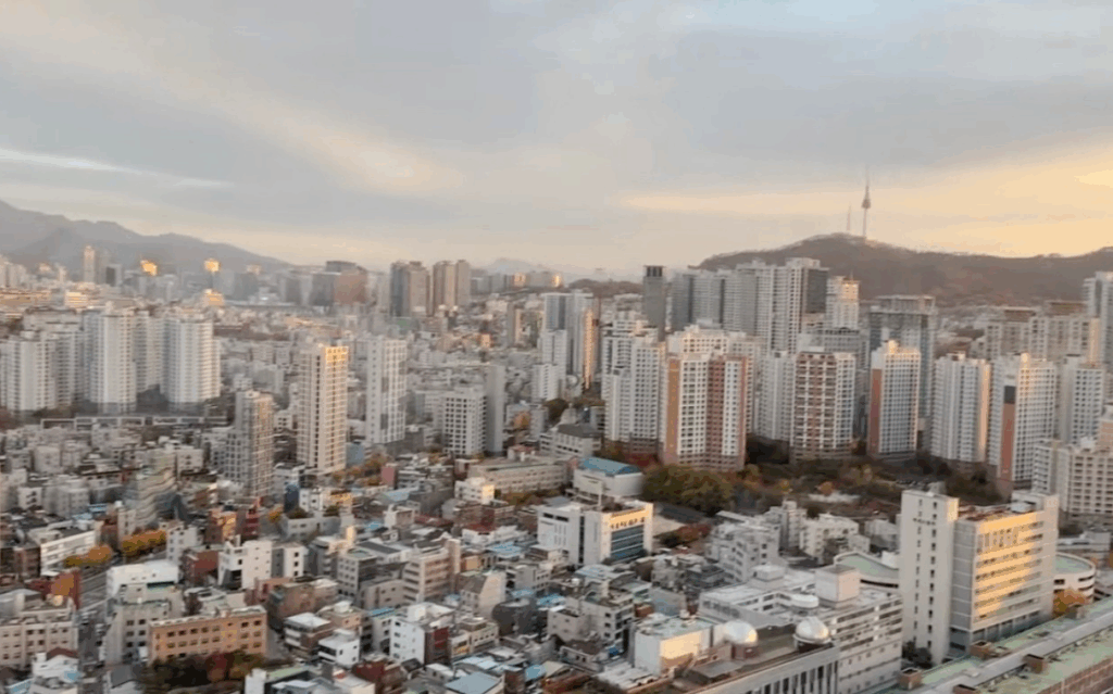 ソウル龍山区ホテル客室からの南山タワー（Nソウルタワー）都市景観 夕暮れの柔らかな光に照らされるソウル中心部の高層ビル群 HYBEビル・龍山駅周辺エリア 晩秋の穏やかな空 K-POP推し活旅行の宿泊先からの眺望