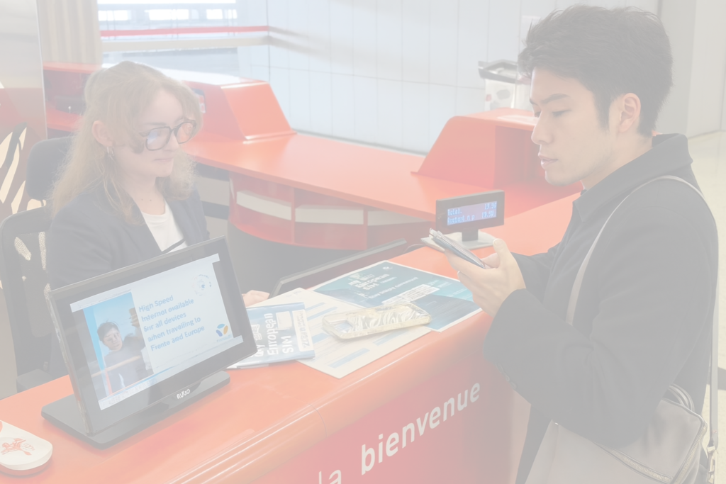 空港のSIMカウンターで手続きをする日本人旅行者とスタッフの様子。海外での通信トラブルのイメージとして、VOYAGEESIMレビュー記事の導入に使用する画像。